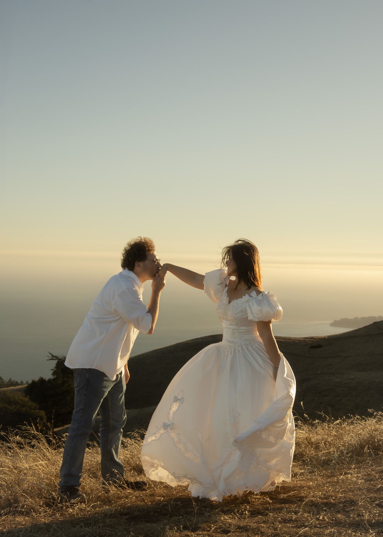 Couple twirling on a golden hillside above the ocean